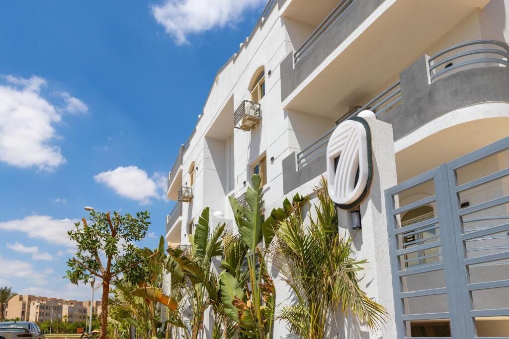 Edifício moderno com varandas, porta de garagem e plantas tropicais.