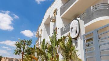 Edifício moderno com varandas, porta de garagem e plantas tropicais.