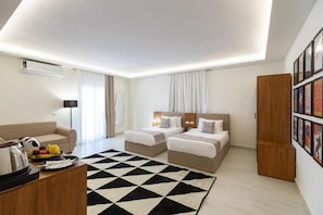 A modern hotel room with two beds, a sofa, a coffee table, and a black-and-white patterned rug.