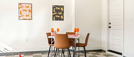 Uma sala de jantar com mesa e cadeiras, uma porta e dois quadros de animais na parede.