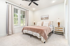 A bedroom with a bed, a nightstand, a lamp, a ceiling fan, and a window with curtains. - The Cottage on College, Brand New Build with Game Room, Sleeps 10 (Auburn)
