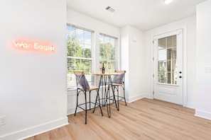 Une chambre moderne avec un plancher en bois, des murs blancs et une porte dotée d’une fenêtre. On y trouve deux chaises et une table sur laquelle sont posés une bouteille et des verres.