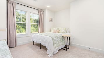 A bedroom with a bed, a bedside table, a window with curtains, and a wall-mounted light fixture.