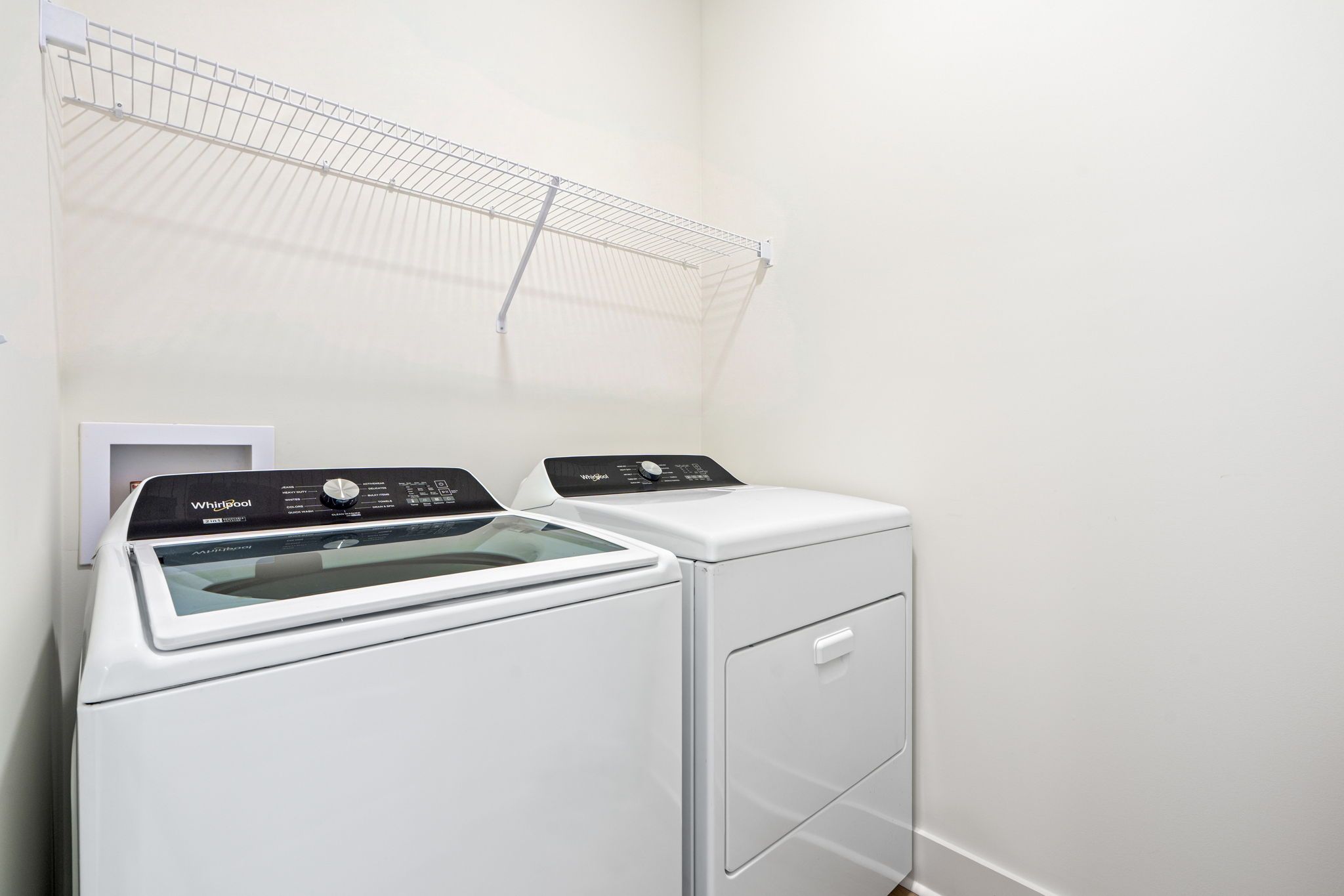 A compact, modern laundry room with a front-loading washer and dryer, a metal drying rack, and a small white cabinet.