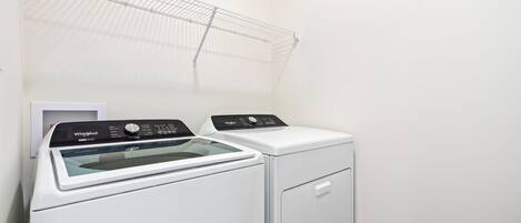 A compact, modern laundry room with a front-loading washer and dryer, a metal drying rack, and a small white cabinet.