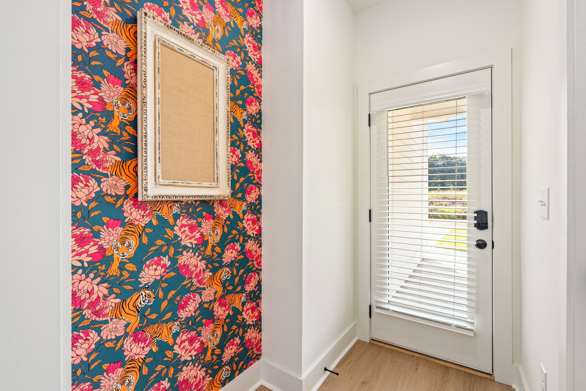 Ein Flur mit einer Tür, die horizontale Jalousien hat, einer Wand mit einem Blumenmuster-Tapete und einem gerahmten Bild an der Wand.