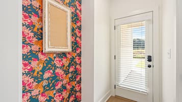 Ein Flur mit einer Tür, die horizontale Jalousien hat, einer Wand mit einem Blumenmuster-Tapete und einem gerahmten Bild an der Wand.