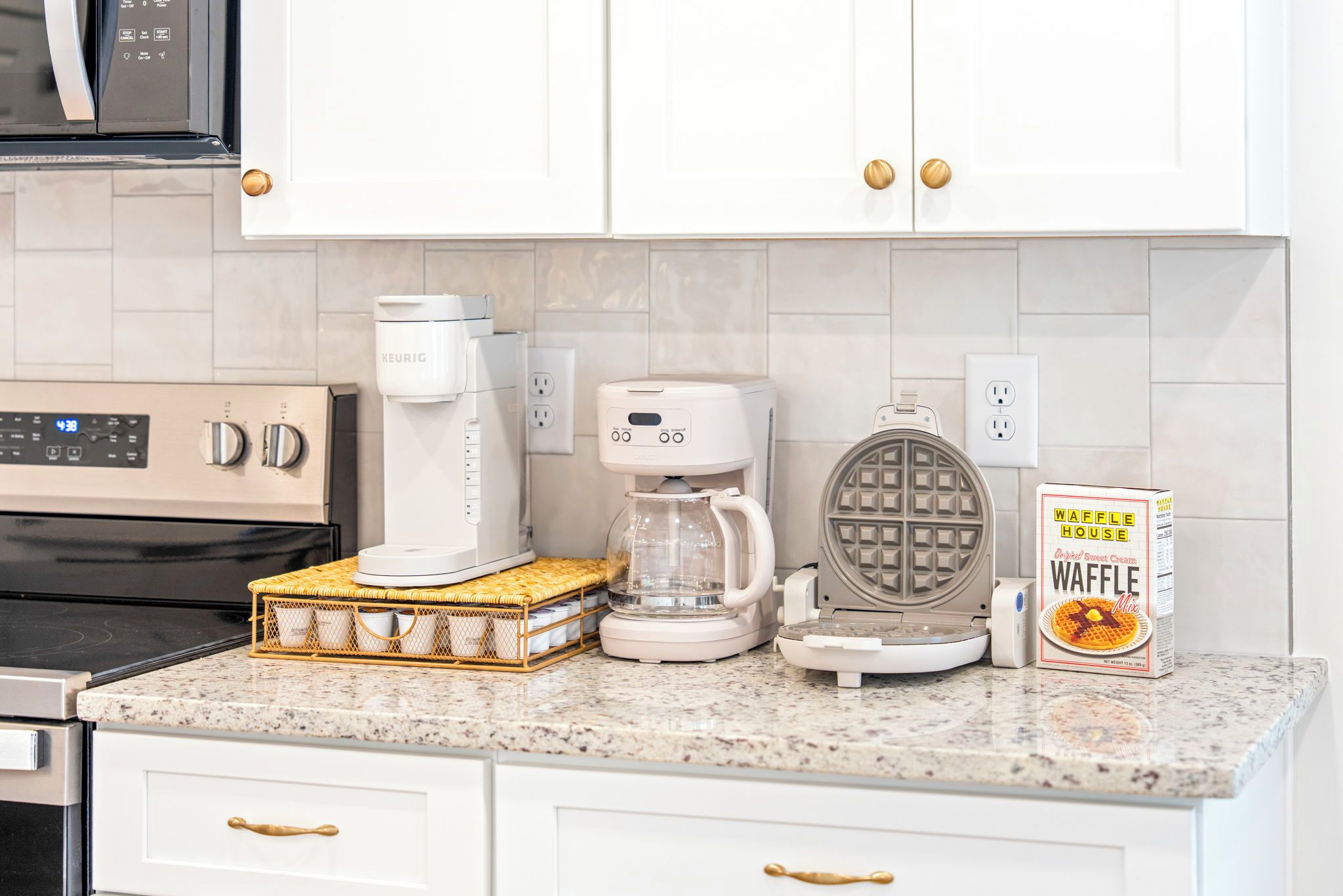 Una cocina con cafetera, máquina para hacer gofres y mezcla para gofres sobre la encimera.