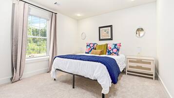 Quarto com cama, mesa de cabeceira, espelho e janela com cortinas.