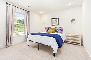 Une chambre à coucher avec un lit, une table de chevet, un miroir et une fenêtre avec des rideaux.
