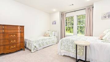 Quarto com duas camas de solteiro, cômoda de madeira, mesa redonda pequena e janela com cortinas.