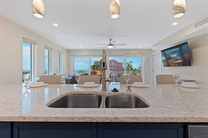A modern kitchen with a central island, stainless steel sink, and a ceiling fan. - 🌴Salty Seahorse Unit 200 | Heated Pool | Steps to Beach🌞 (Fort Myers Beach)
