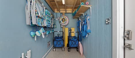 Un pasillo estrecho con techo de madera, una pared azul y varios objetos como un flotador, un cochecito azul y un carrito para bebé.
