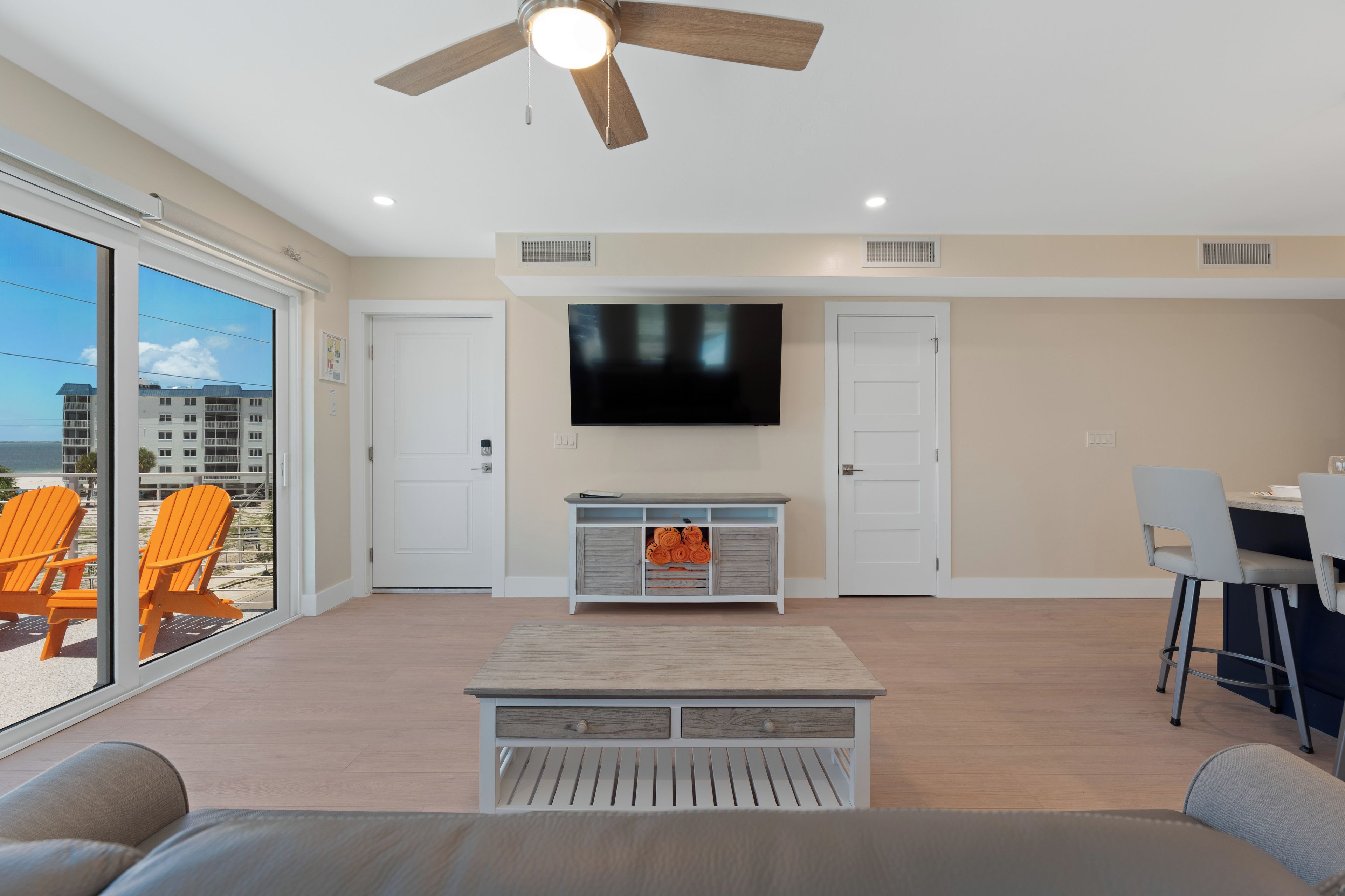 A spacious living room with a ceiling fan, a flat-screen TV mounted on the wall, and a dining area with a table and chairs.