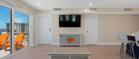 A spacious living room with a ceiling fan, a flat-screen TV mounted on the wall, and a dining area with a table and chairs.