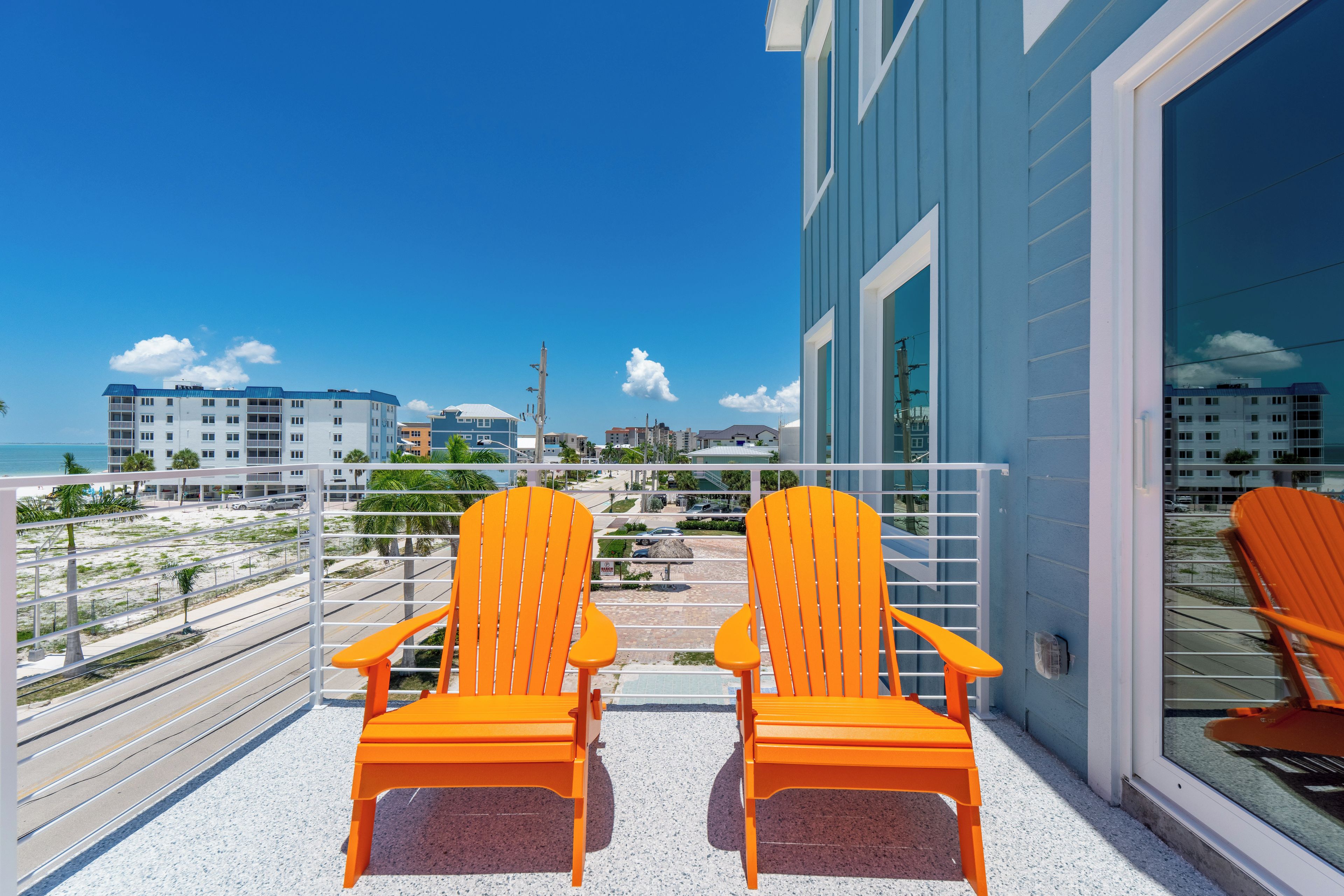 A balcony with two orange chairs facing a beach view, a clear sky, and a distant water tower.
