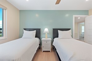 A bedroom with two beds, a nightstand with a lamp, and a ceiling fan. - 🌴Salty Seahorse Unit 200 | Heated Pool | Steps to Beach🌞 (Fort Myers Beach)