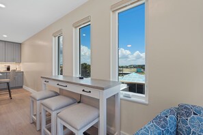 A modern kitchen with a built-in island, a dining area with a bench, and large windows offering a view of the cityscape. - 🌴Salty Seahorse Unit 200 | Heated Pool | Steps to Beach🌞 (Fort Myers Beach)