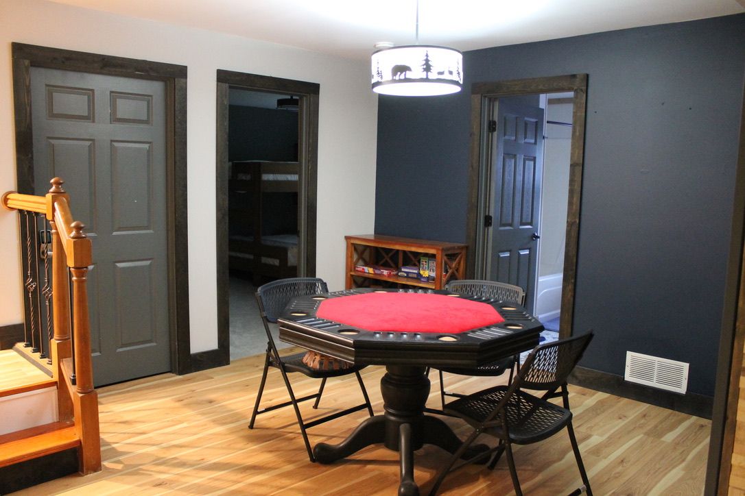 Una habitación con una mesa redonda, cuatro sillas, un cojín rojo, una mesita de madera y una araña.
