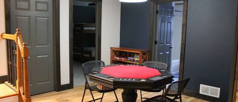 Una habitación con una mesa redonda, cuatro sillas, un cojín rojo, una mesita de madera y una araña.