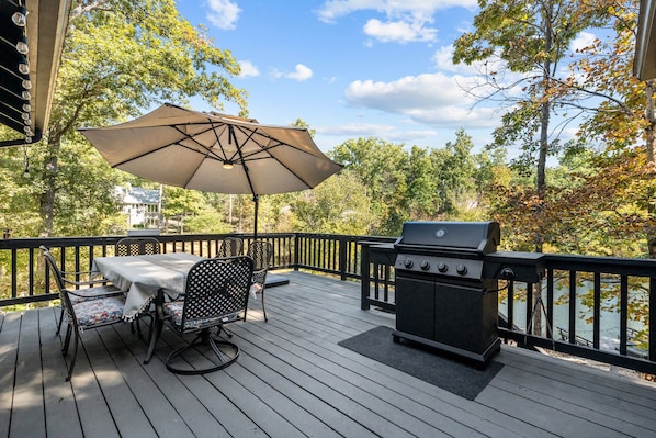 A deck with a grill and outdoor furniture, overlooking a body of water.