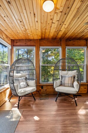 Una habitación con dos sillones de mimbre con cojines, paredes de madera y ventanas grandes.