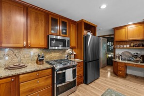 A kitchen with wooden cabinets, stainless steel appliances, granite countertops, and a wooden floor.