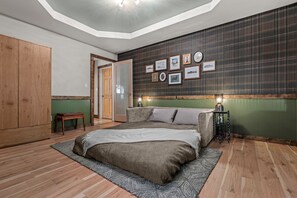 A bedroom with a bed, a bench, a wall with framed pictures, and a door.
