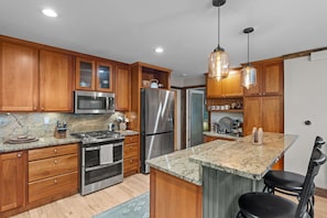 A modern kitchen with wooden cabinets, stainless steel appliances, granite countertops, and pendant lighting.