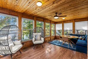 Una habitación acogedora con paredes de madera, ventanas grandes, ventilador de techo y un sofá azul.