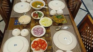 Una mesa de comedor dispuesta con platos, tazones y cubiertos, rodeada de sillas.