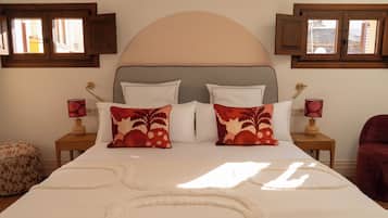 Una cama con cabecera, dos mesitas de noche con lámparas y una ventana con cortinas.