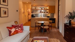 A compact living space with a sofa, a dining table with chairs, a kitchen area, and a small side table with a tray. - Casa Roca - Palma Old Town Wine Hotel (Palma)