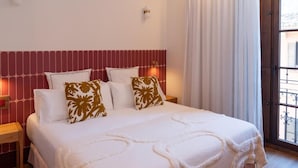 A bed with a white bedspread and decorative pillows, a bedside table with a lamp, and a window with curtains. - Casa Roca - Palma Old Town Wine Hotel (Palma)