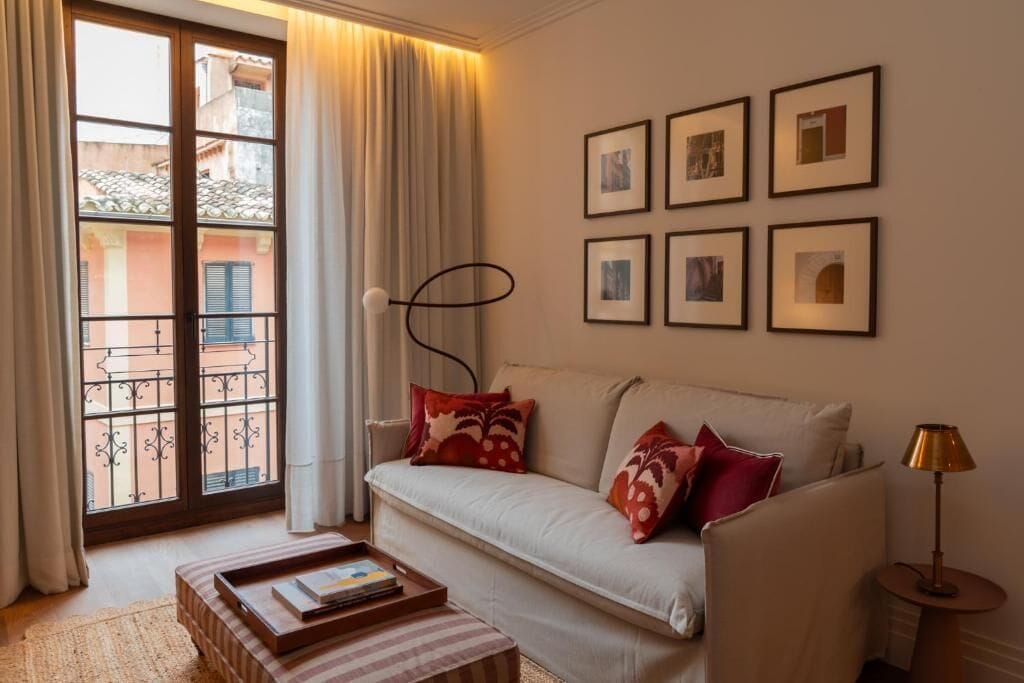 A living room with a sofa, a coffee table, a lamp, and a window with a view of buildings.