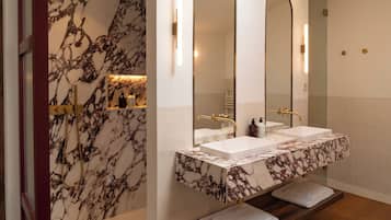 Un baño con paredes de mármol, un lavamanos doble y un espejo grande.