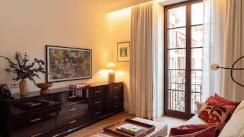 A well-lit living room with a sofa, a coffee table with books, a cabinet, a painting, and a window with curtains.