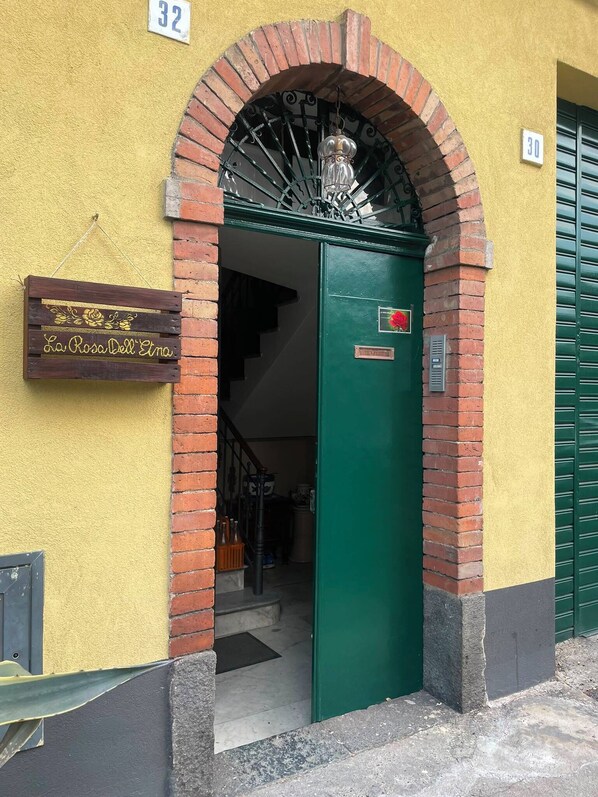 Een gevelingang met een groene deur, een bakstenen boog en een bord met de tekst 'La Rosa Dell'Enzo'.
