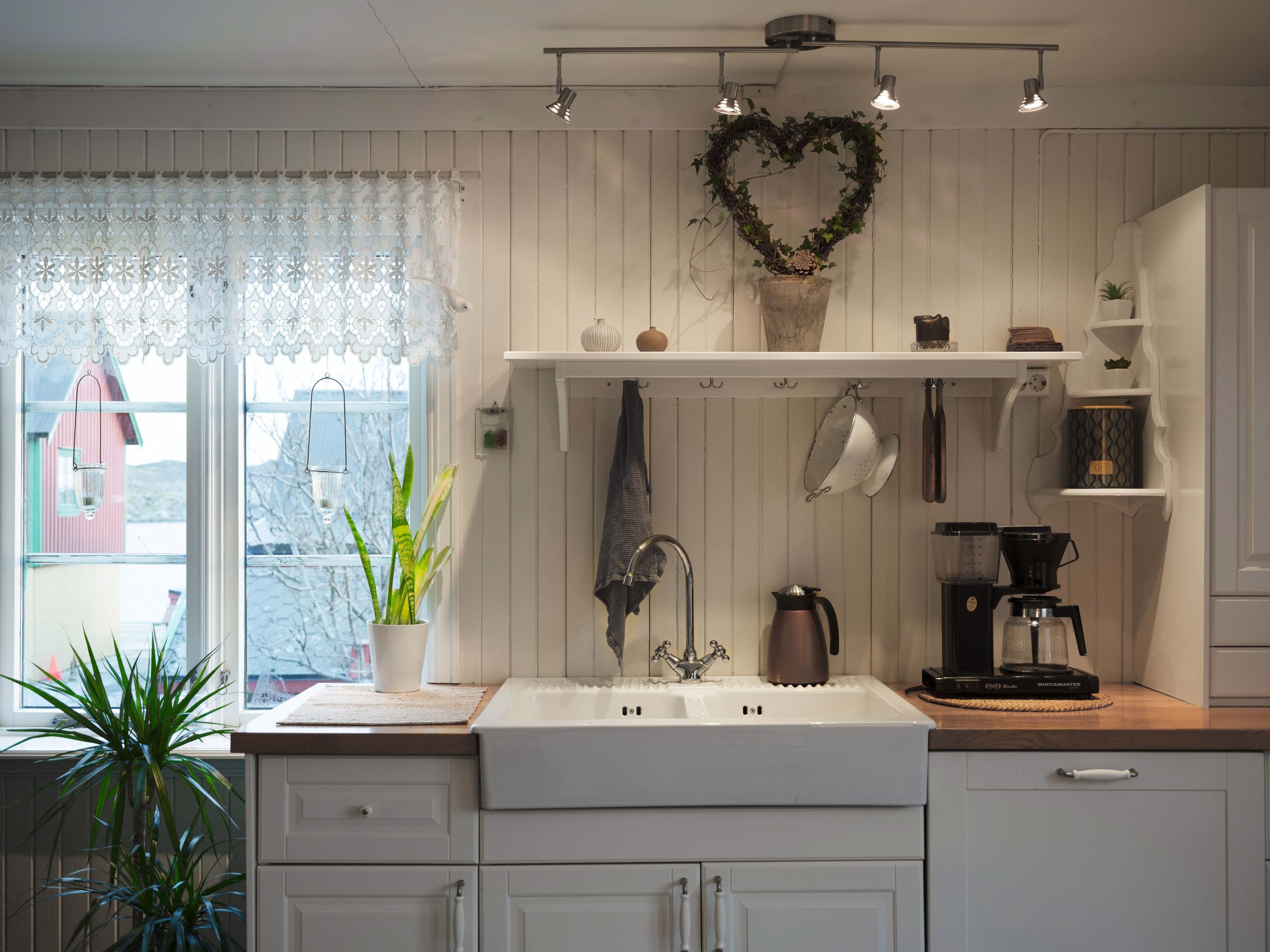 A kitchen with a white sink, a coffee maker, and a heart-shaped decoration on the wall.