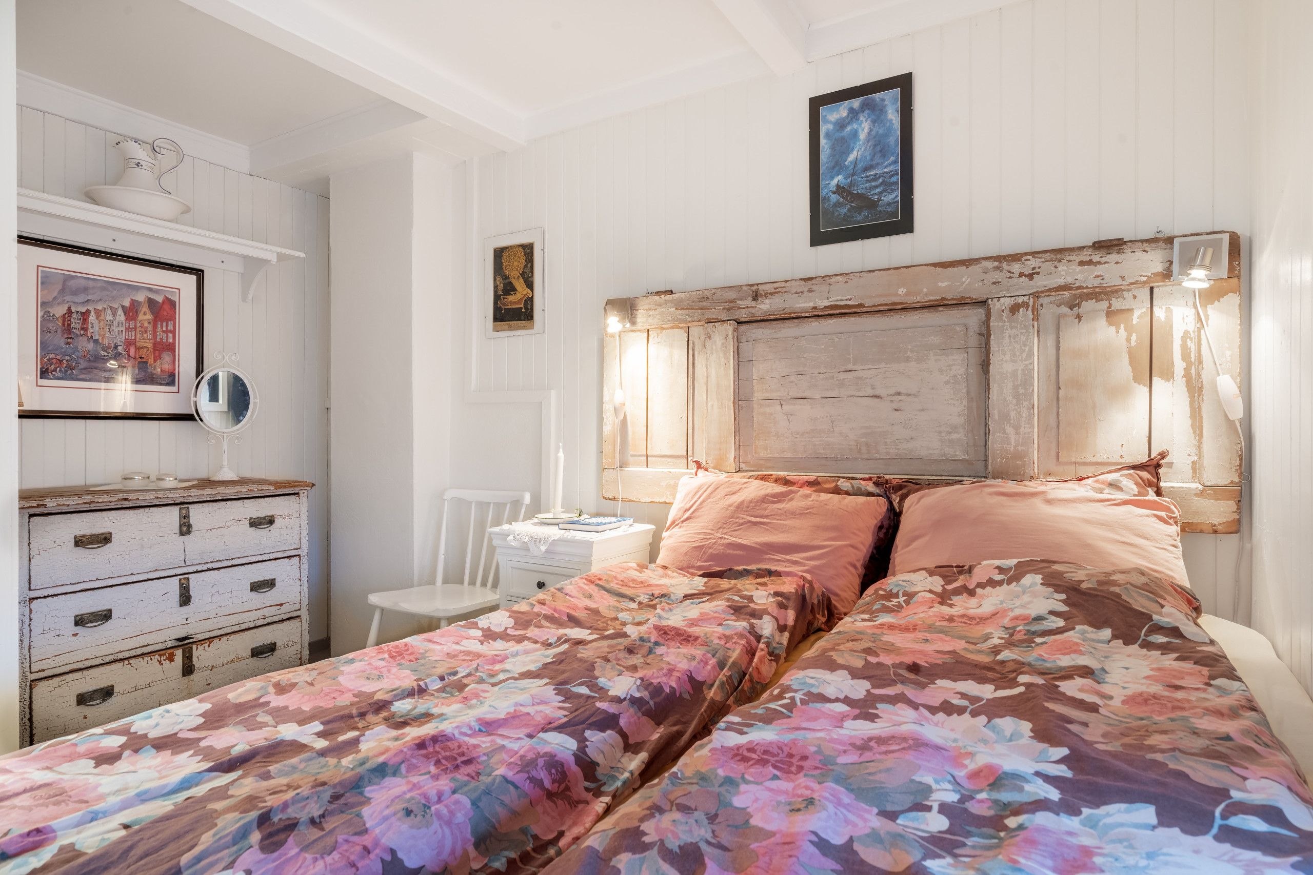 A bedroom with a bed, a dresser, a chair, and a wall-mounted lamp.