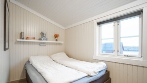 A bedroom with a bed, a window, and a shelf with books and a vase. - Cozy seaside cabin in Stamsund (Stamsund)