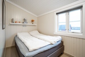 A bedroom with a bed, a window, and a shelf with books and a vase. - Cozy seaside cabin in Stamsund (Stamsund)