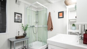 A modern bathroom with a glass-enclosed shower, a white sink, and a small table with a vase. - Cozy seaside cabin in Stamsund (Stamsund)