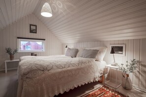 Un dormitorio con una cama grande, una mesita de noche, una lámpara, una ventana y una planta.