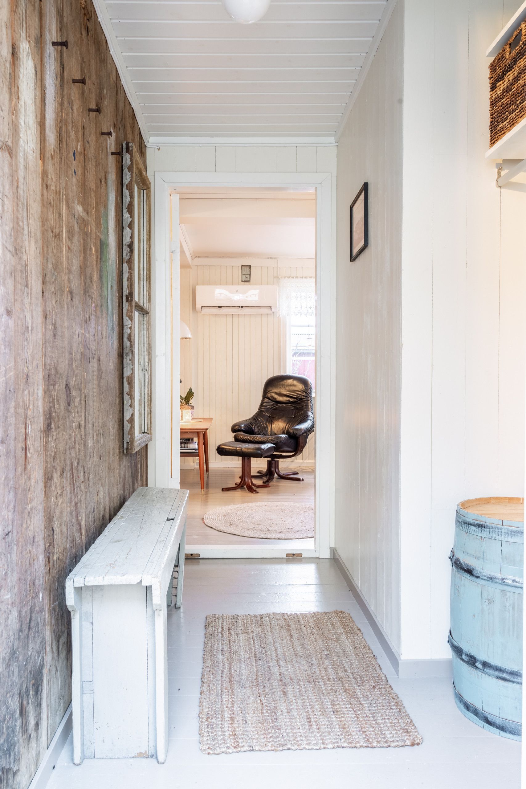 A hallway with a wooden bench, a rug, and a blue barrel.