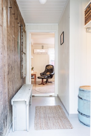 A hallway with a wooden bench, a rug, and a blue barrel.