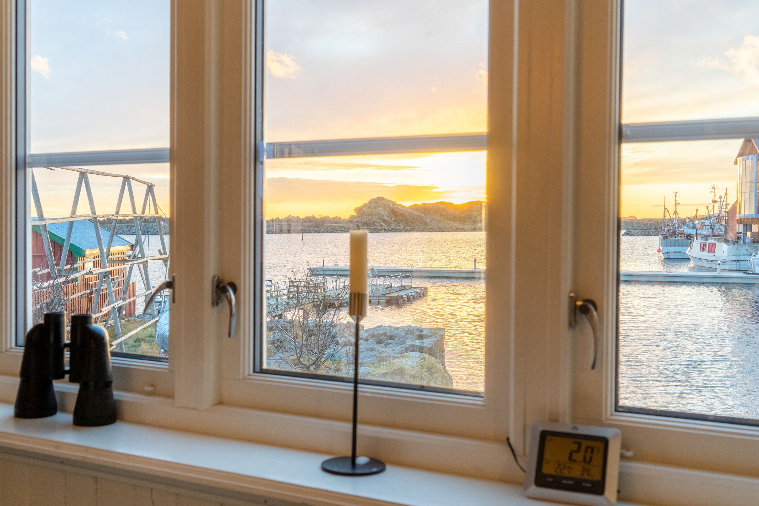 A window with a view of a harbor, a clock, and a pair of binoculars on a windowsill.
