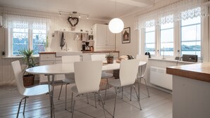 A modern kitchen with white cabinetry, a dining table with chairs, and a view of the outdoors through large windows. - Cozy seaside cabin in Stamsund (Stamsund)
