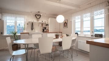 A modern kitchen with white cabinetry, a dining table with chairs, and a view of the outdoors through large windows.