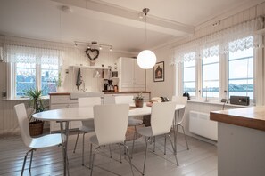 A modern kitchen with white cabinetry, a dining table with chairs, and a view of the outdoors through large windows. - Cozy seaside cabin in Stamsund (Stamsund)